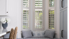 updated-built-in-window-seat-bench-fixed-beneath-bay-windows-covered-in-white-shutters