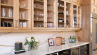 Waypoint-cabinetry-made-from-maple-wood-in-a-Rye-finish-upper-cabinets-include-clear-glass-inserts-plus-additional-cabinetry-above-for-storage