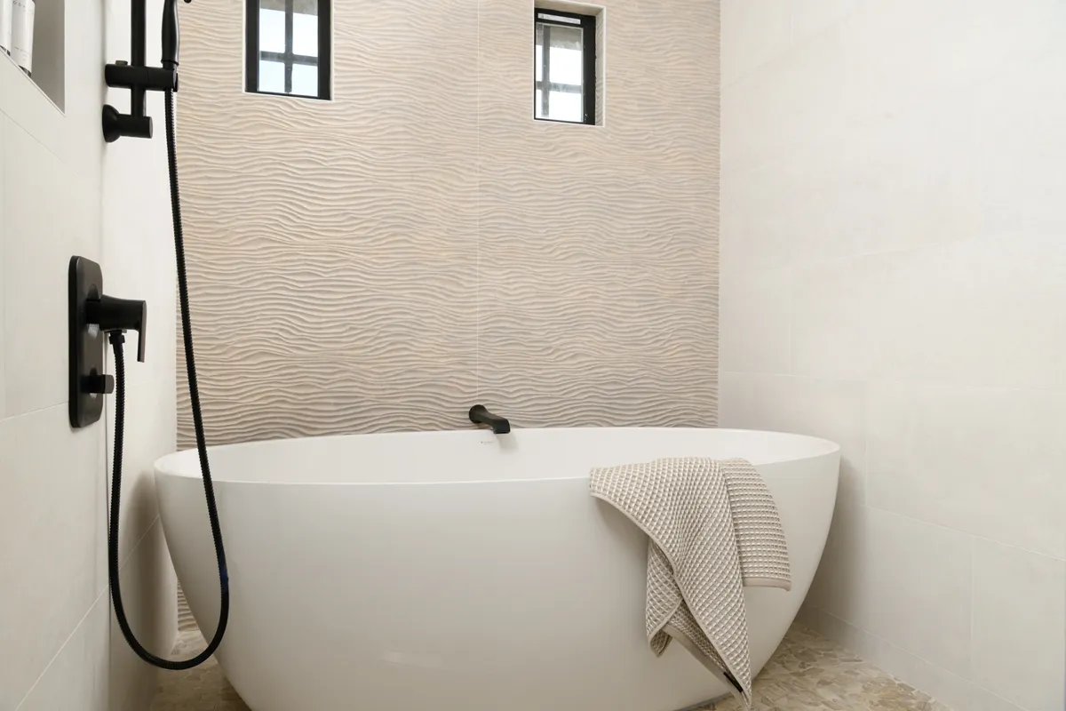 white-Fleurco-Grande-soaking-tub-sits-in-front-of-textured-three-dimensional-wavy-accent-wall-in-Hawi-natural-finish
