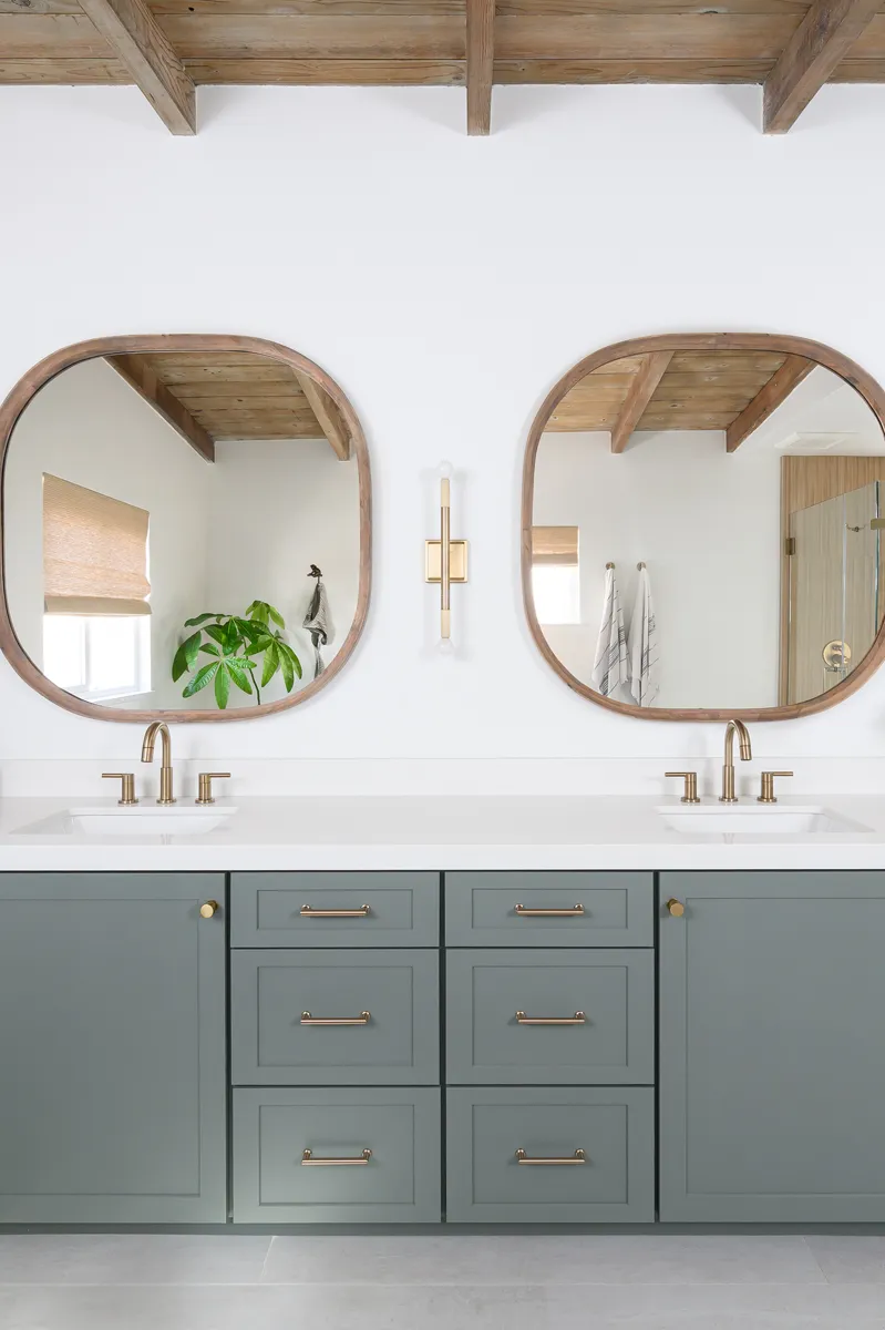 two-wood-framed-mirrors-and-two-champagne-bronze-light-wall-sconces-sit-above-the-Ocean-Foam-quartz-vanity-countertops