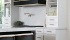 custom-sloped-appliance-hood-in-black-with-brass-strappings-sit-above-a-Wolf-range-and-satin-gold-pot-filler